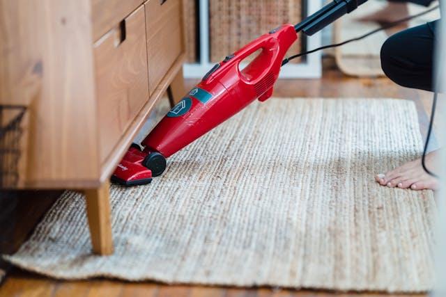 Woman vacuuming under a wooden cabinet with a red vacuum.