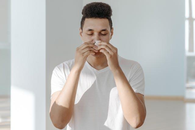 A man in a white shirt sneezing and wiping his nose with a napkin.